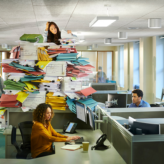 woman overwhelmed with piles of paperwork on desk