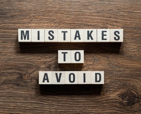 Wooden blocks spelling out 'Mistakes to Avoid' on a table, symbolizing the importance of strategies to avoid compliance mistakes in Title IV financial aid.