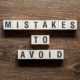 Wooden blocks spelling out 'Mistakes to Avoid' on a table, symbolizing the importance of strategies to avoid compliance mistakes in Title IV financial aid.